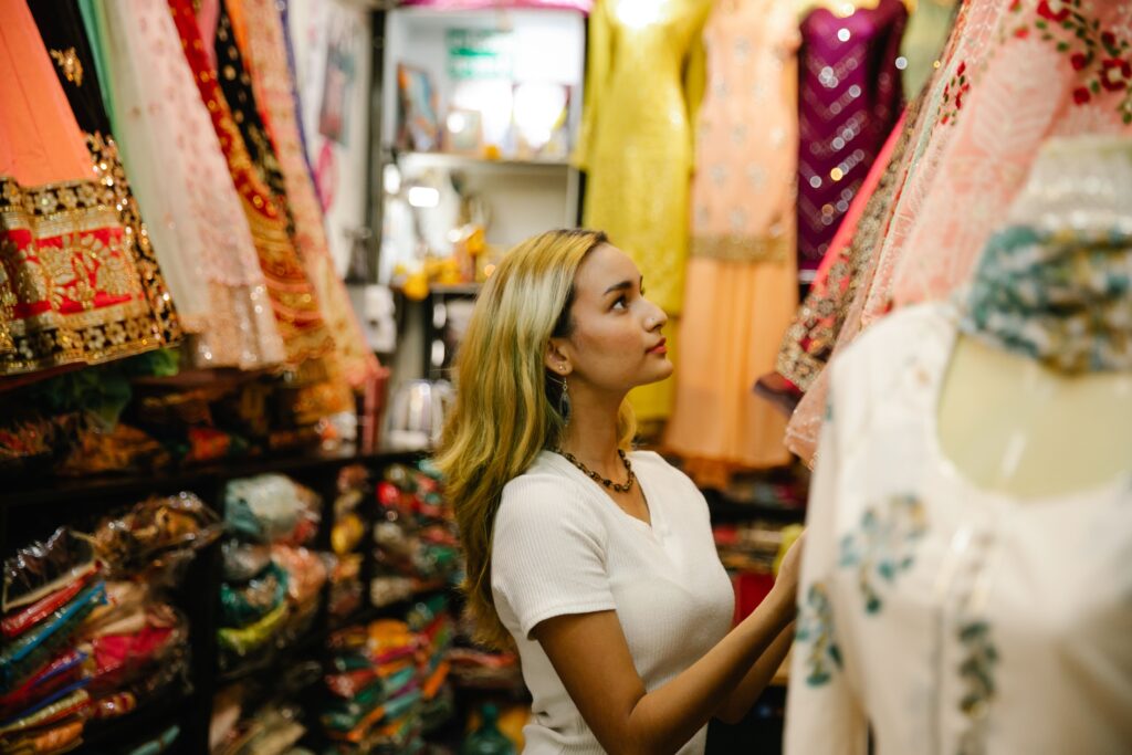 Woman explores colorful traditional dresses in a boutique, surrounded by diverse fabrics and patterns.